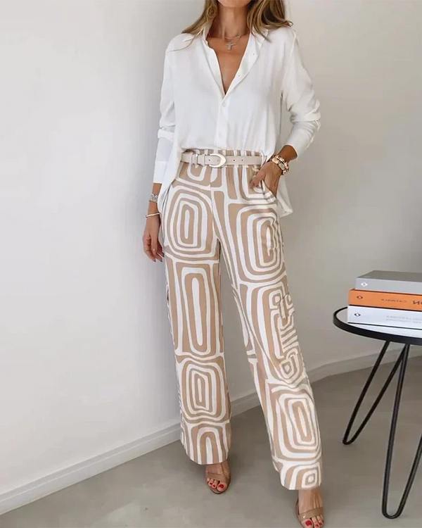 A woman wearing a plain button-up top with geometric-print trousers and a belt at the waist.