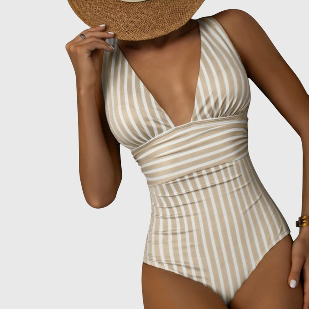 A woman walking by the sea in a bright printed swimsuit, relaxed and glowing in the sun.