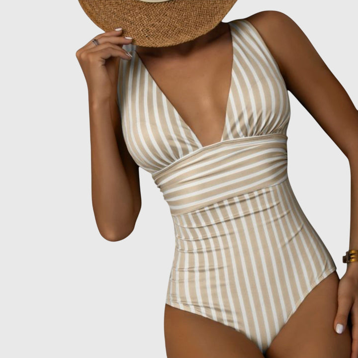 A woman walking by the sea in a bright printed swimsuit, relaxed and glowing in the sun.