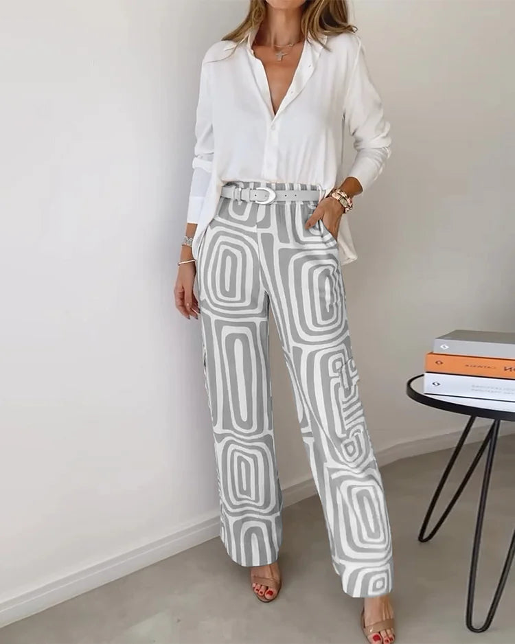 A woman wearing a plain button-up top with geometric-print trousers and a belt at the waist.