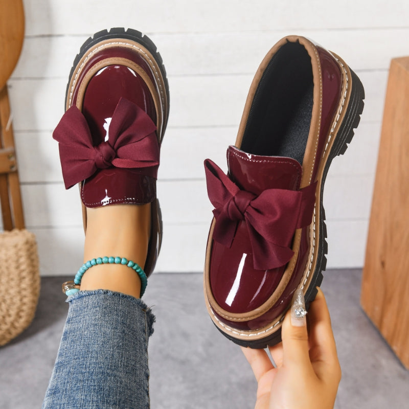 Green and black glossy loafers with a bold bow detail at the front