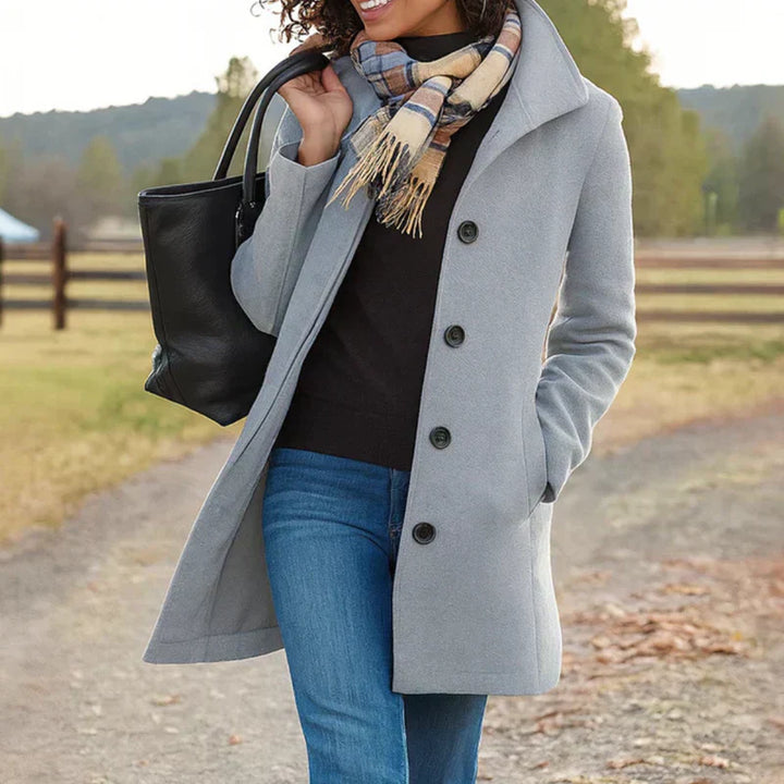 A woman wearing an elegant single-button coat over a jumper on a crisp autumn day.