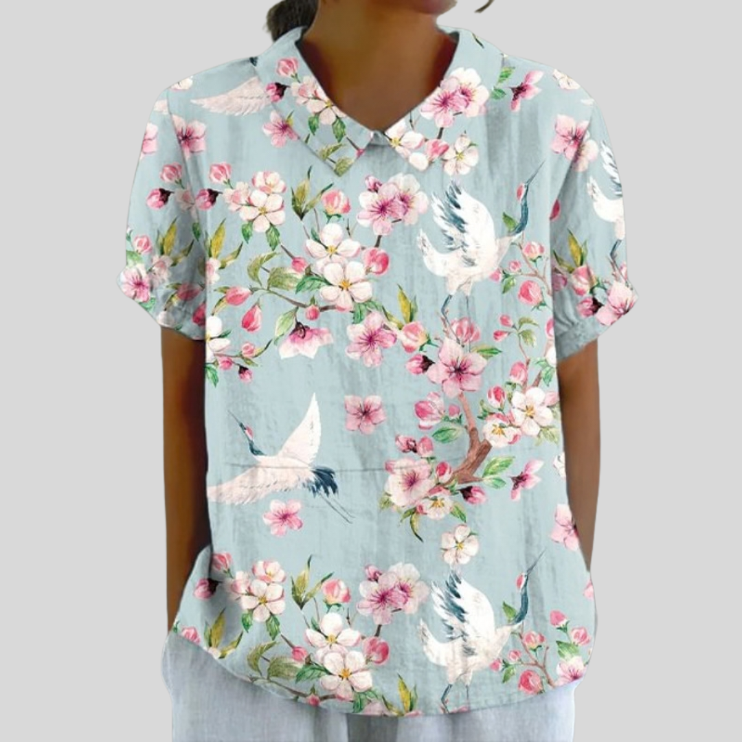 A woman wearing a flowing floral top with a polo collar, looking feminine and self-assured.