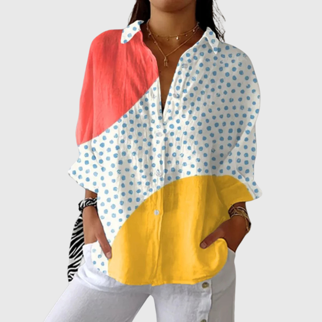 A woman wearing a loose colourful printed blouse with an elegant button front, styled with trousers for a relaxed day out.