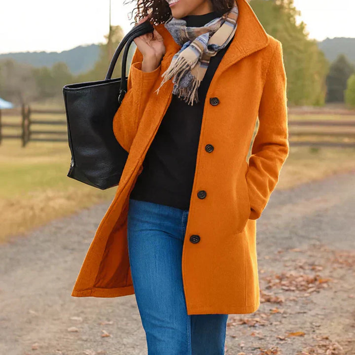A woman wearing an elegant camel button-through coat over a jumper on a crisp autumn day.