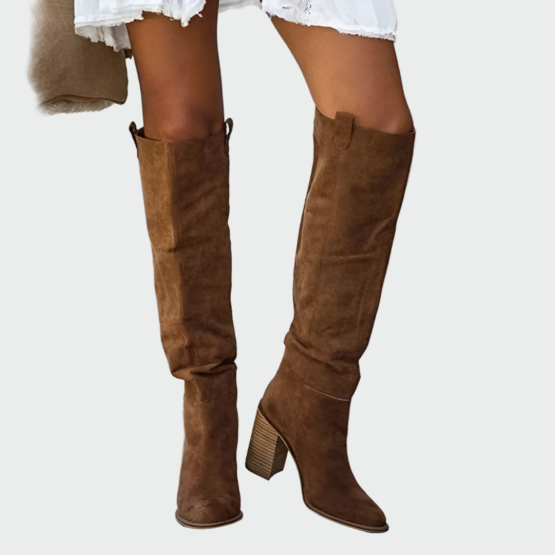 A woman in a dress wearing warm brown Western-style ankle boots with a sturdy heel.