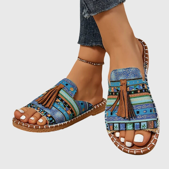 A woman wearing colourful patterned boho slides with tassel details on a holiday day out.