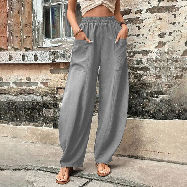 A woman walking in flowing wide-leg trousers with big patch pockets and an elegant, draped silhouette.