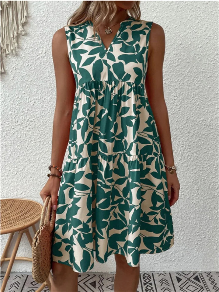 Woman wearing the Eileen sleeveless leaf-print midi dress in green, relaxing outdoors on a warm afternoon.
