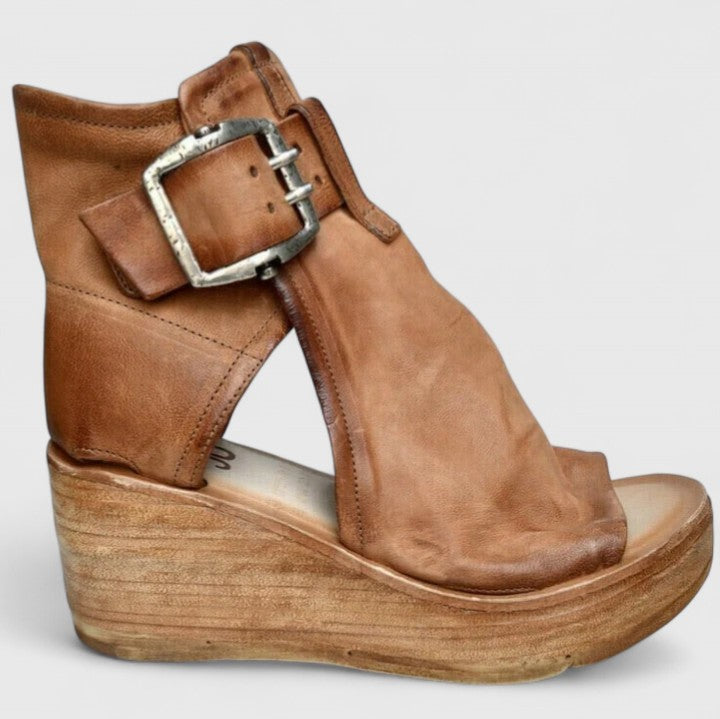 A woman in tan buckle wedge sandals, walking easily on a summer afternoon.