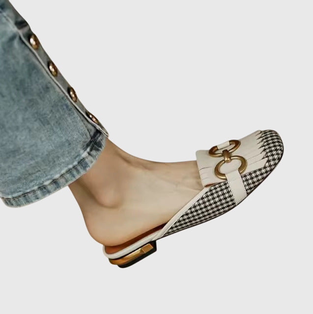 A cream closed-toe mule with a gold horsebit ring detail and a low heel.