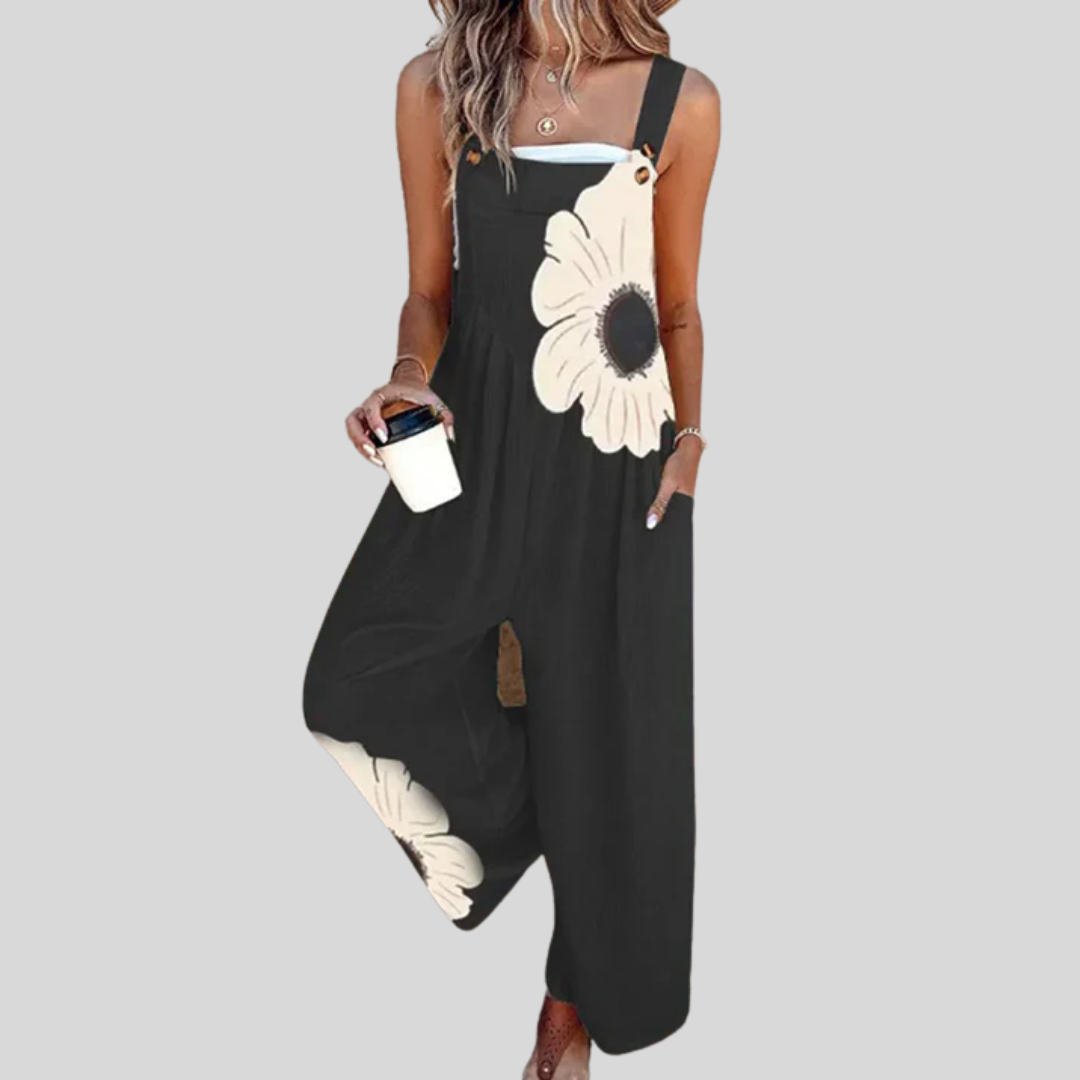 Woman wearing the Aoife™ black wide-leg dungarees with two large cream sunflower blooms printed across the full front, from bib to lower leg.