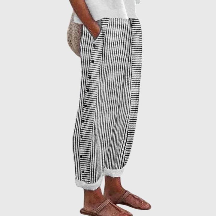 A woman wearing elegant everyday trousers in a fine blue stripe with a wide cut and side buttons.