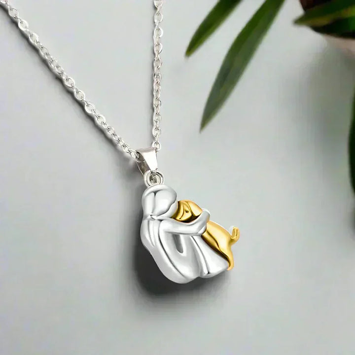 Gold pendant necklace showing a person and dog in a tender embrace