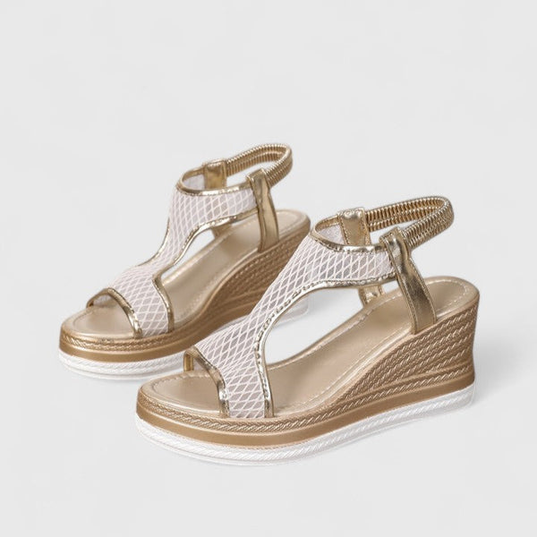 A woman wearing golden platform wedge sandals with a T-bar front, open-weave panels and a stretchy slingback.