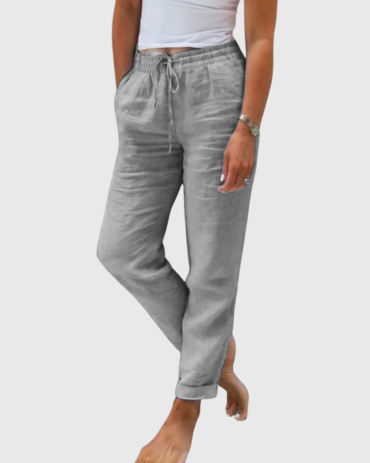 Woman wearing tailored trousers with a smart top, standing confidently in soft light.