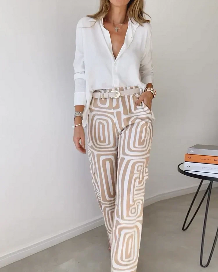 A woman wearing a plain button-up top with geometric-print trousers and a belt at the waist.