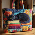 Quilted tote bag with a black cat perched beside a stack of books and a steaming cup of tea