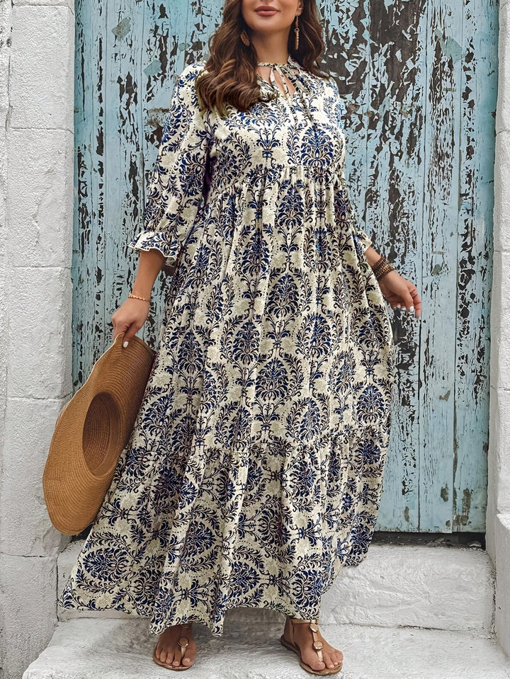 Woman strolling by the sea in the Harriet mosaic print maxi dress with a keyhole neckline and bow detail.