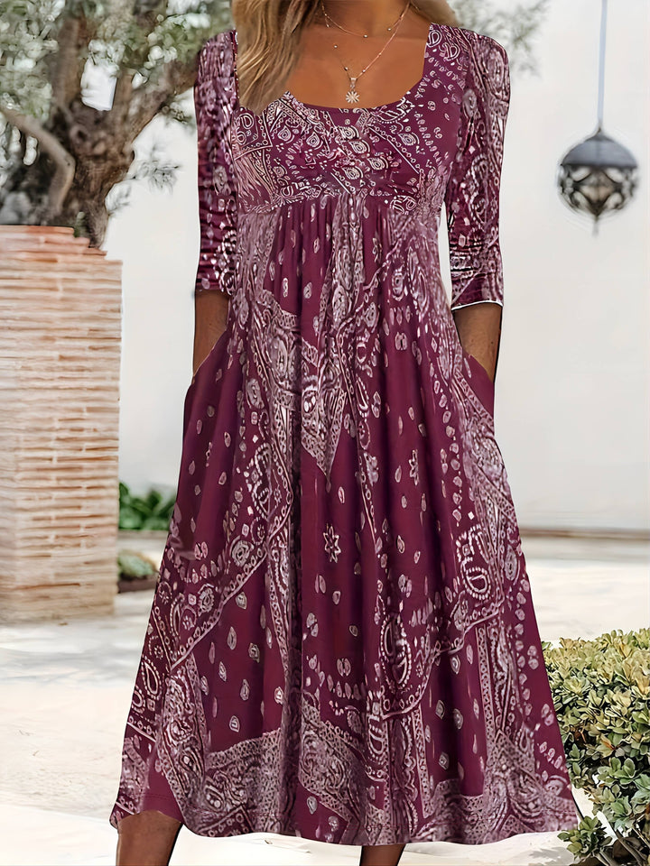 A woman wearing the Maureen long sleeve grey paisley midi dress with a square neckline and flowing skirt, styled for a relaxed day out.