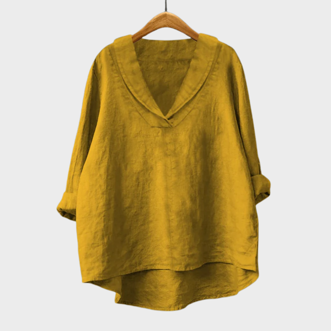 A woman wearing an elegant plain summer blouse with a flowing drape, styled with trousers.