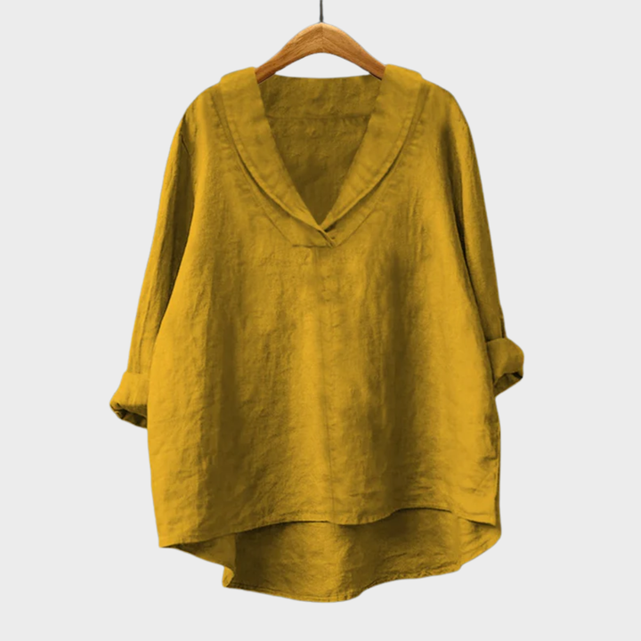 A woman wearing an elegant plain summer blouse with a flowing drape, styled with trousers.