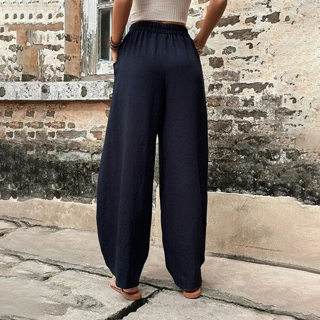 A woman walking in flowing wide-leg trousers with big patch pockets and an elegant, draped silhouette.