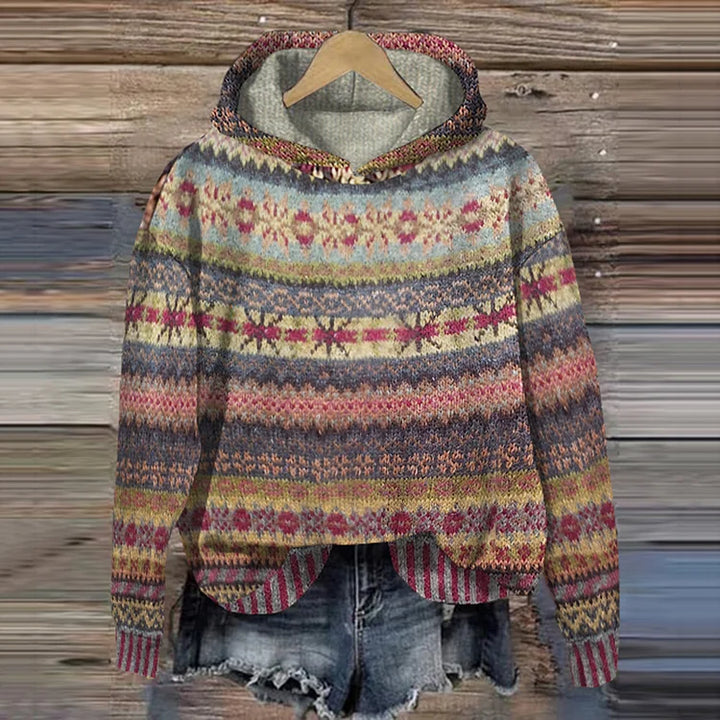 A woman wearing a retro hooded jumper in warm tones with a colourful Nordic pattern.