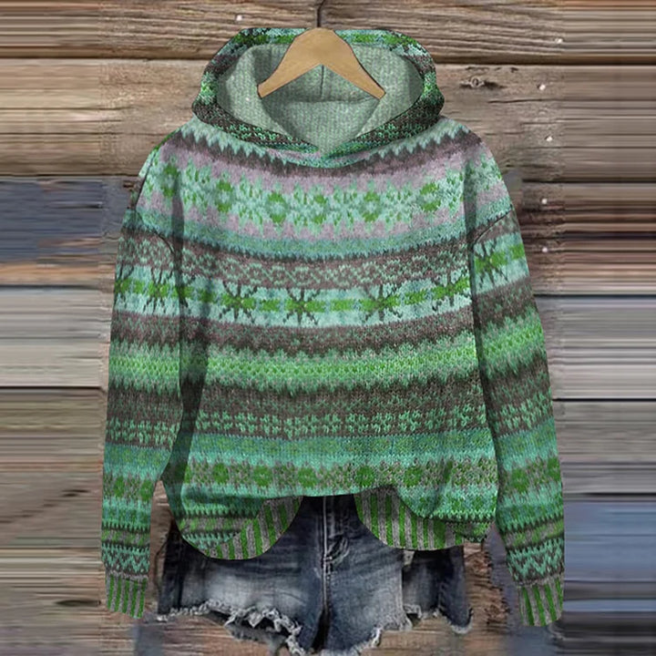 A woman wearing a retro hooded jumper in warm tones with a colourful Nordic pattern.