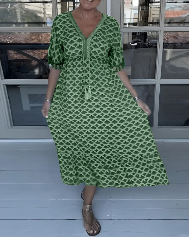 A woman walking near the coast in a flowing blue diamond-lattice print maxi dress with a tassel-trimmed neckline.