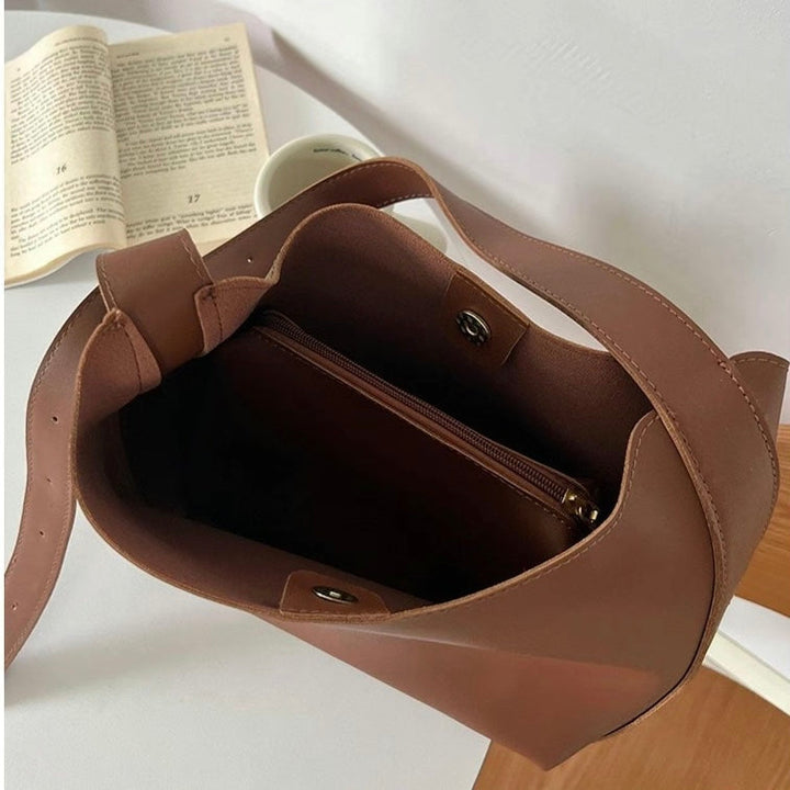 A tan bucket-style shoulder bag with an adjustable buckled strap