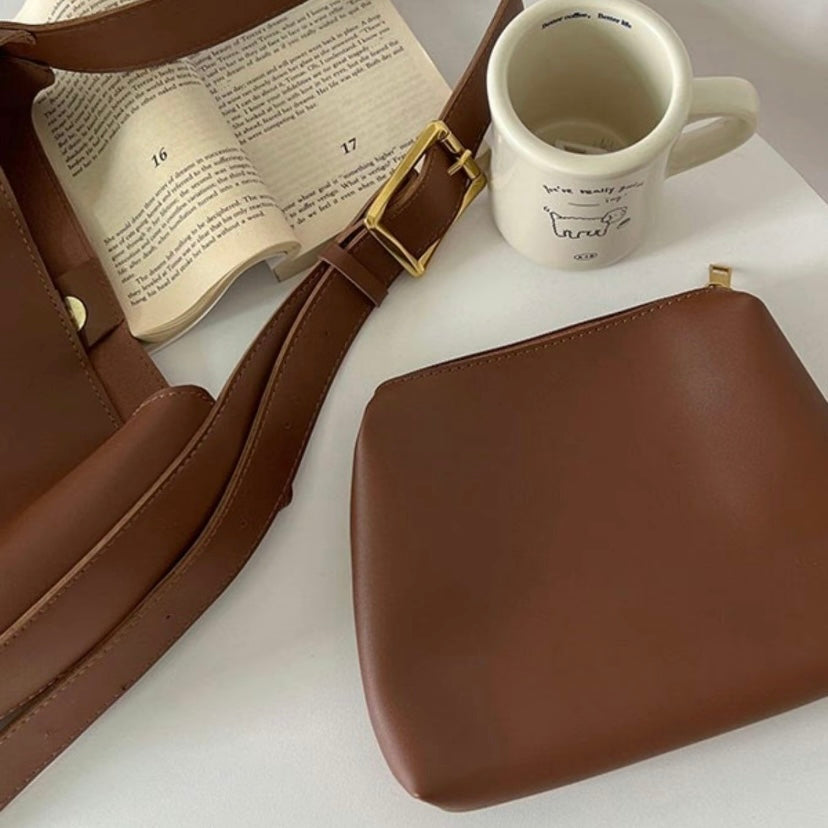 A tan bucket-style shoulder bag with an adjustable buckled strap
