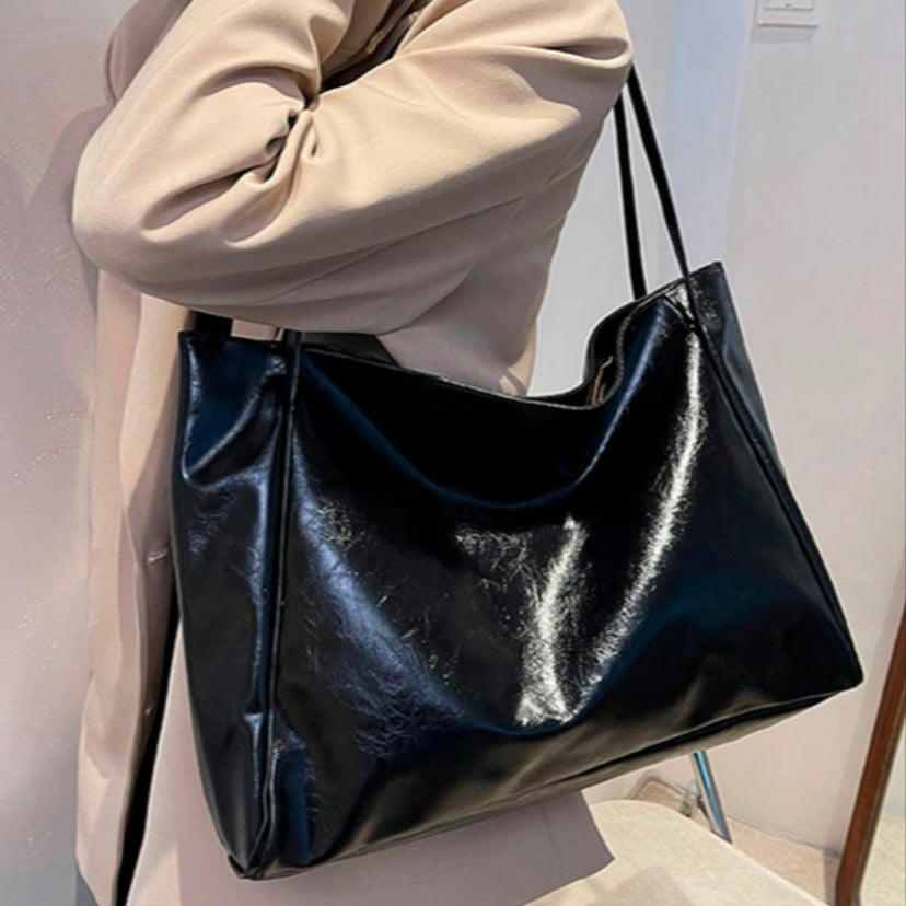 A woman holding a glossy taupe handbag on her arm at an evening occasion.