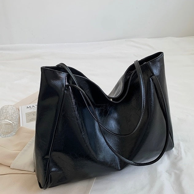 A woman holding a glossy taupe handbag on her arm at an evening occasion.