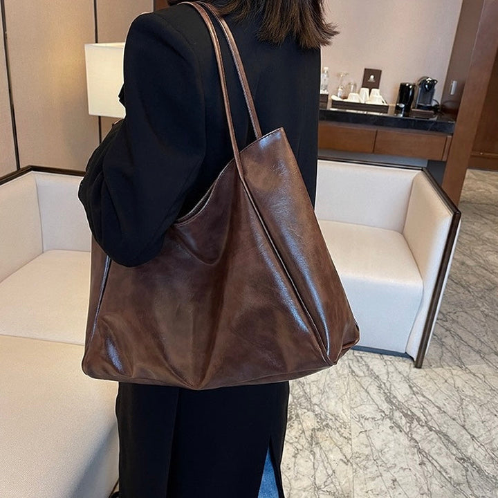 A woman holding a glossy taupe handbag on her arm at an evening occasion.