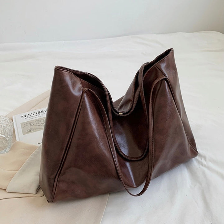 A woman holding a glossy taupe handbag on her arm at an evening occasion.