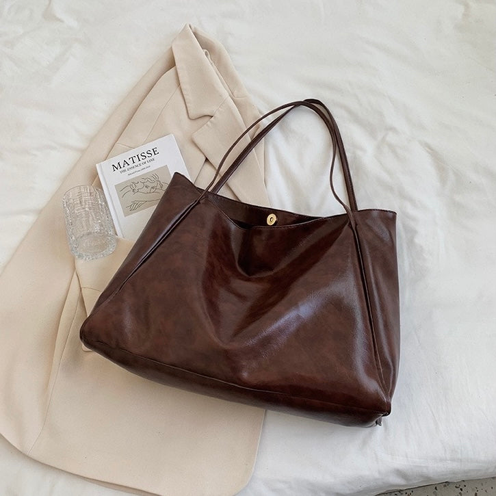A woman holding a glossy taupe handbag on her arm at an evening occasion.