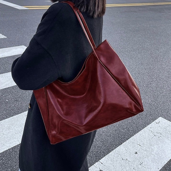 A woman holding a glossy taupe handbag on her arm at an evening occasion.