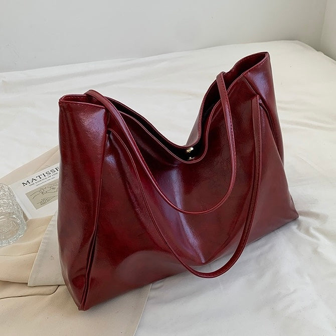 A woman holding a glossy taupe handbag on her arm at an evening occasion.