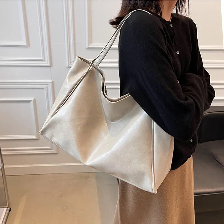 A woman holding a glossy taupe handbag on her arm at an evening occasion.