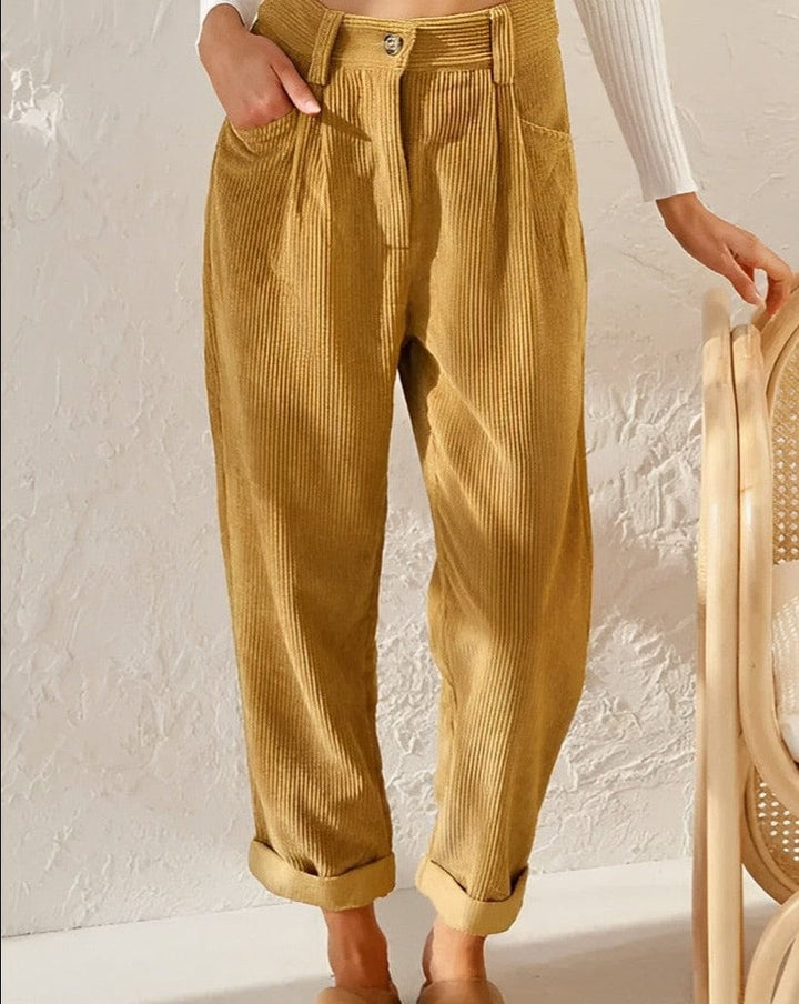 Woman wearing loose high-waisted trousers with a tucked-in top, standing in soft light.