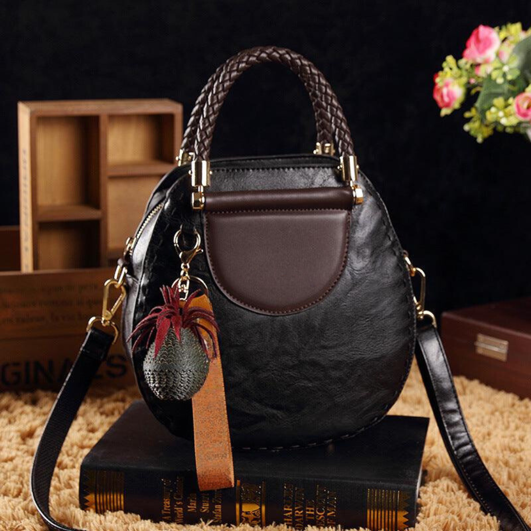 A woman carrying a small round top-handle handbag with a rich finish