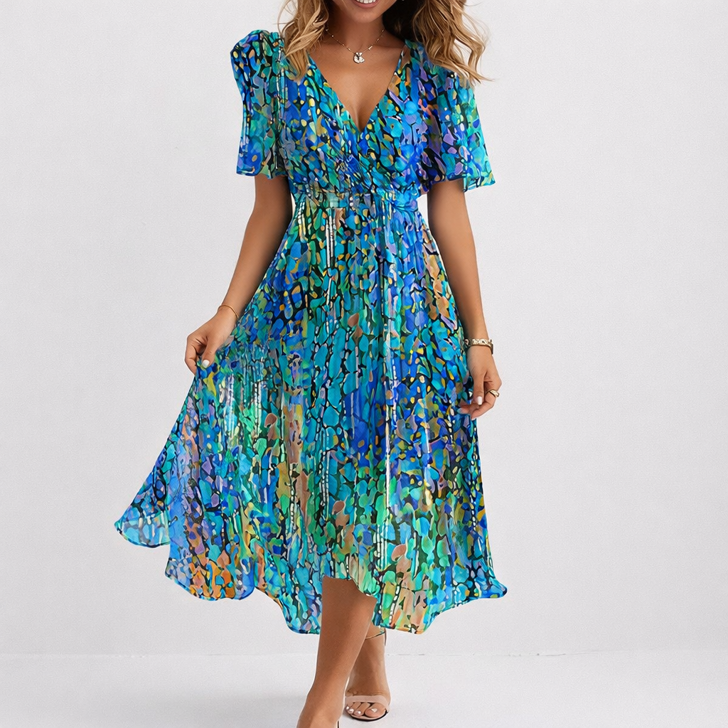 Woman wearing the Hannah airy blue midi dress, the asymmetric hem catching the breeze by the sea.