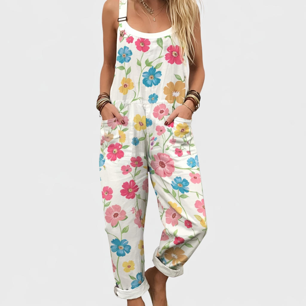 Woman wearing cream dungarees scattered with small pink, blue and yellow flowers, adjustable straps, cheerful and relaxed.