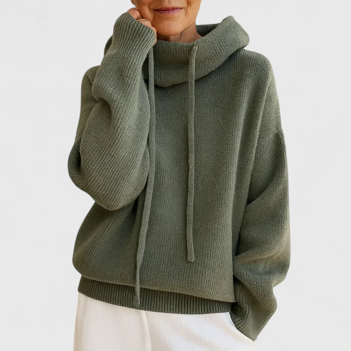 A woman wearing a cosy soft green hoodie with a drawstring hood and white trousers.