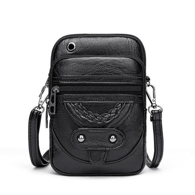 A woman holding a structured black top-handle handbag by the handle at a smart occasion.