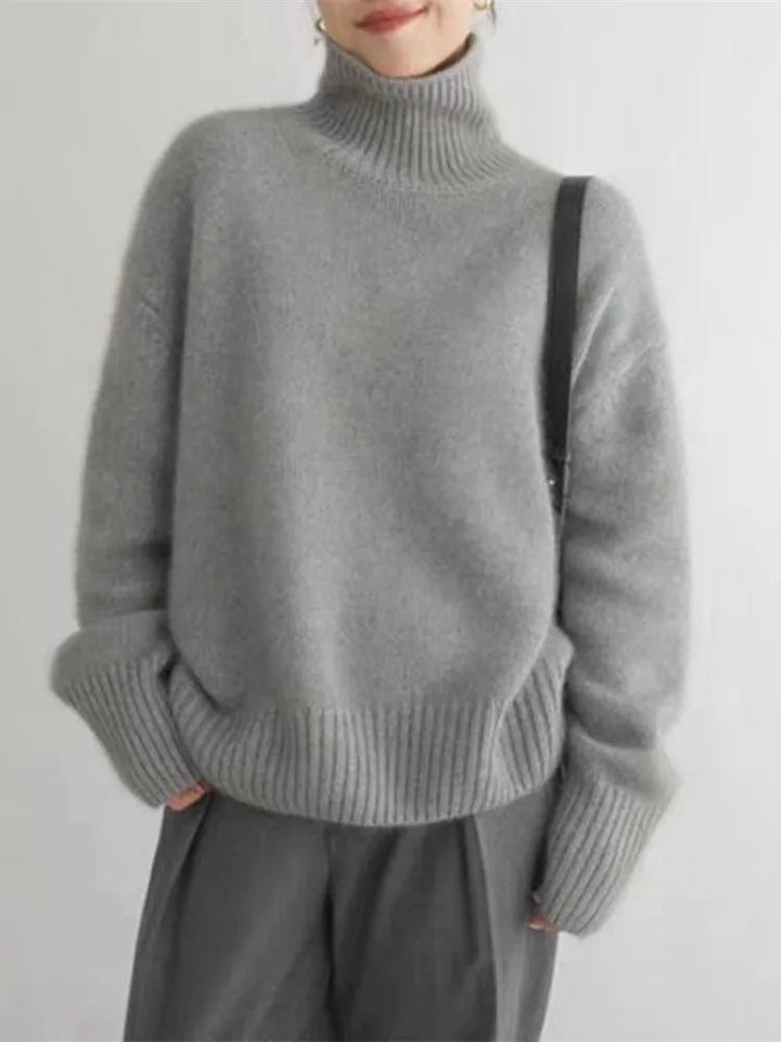 A woman wearing a beige roll-neck jumper, relaxed and warm, paired with trousers.