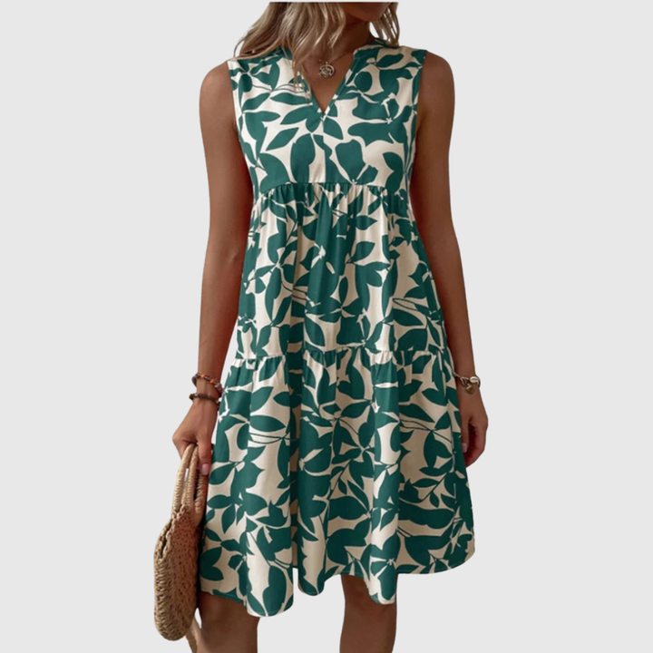 Woman wearing the Eileen sleeveless leaf-print midi dress in green, relaxing outdoors on a warm afternoon.
