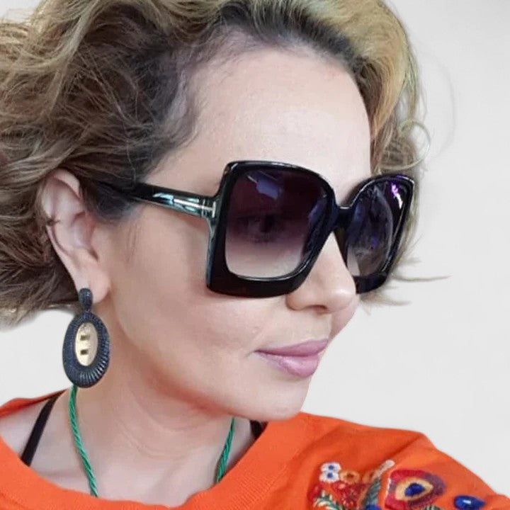 A woman on a sunny day wearing oversized gradient sunglasses, poised and glamorous.