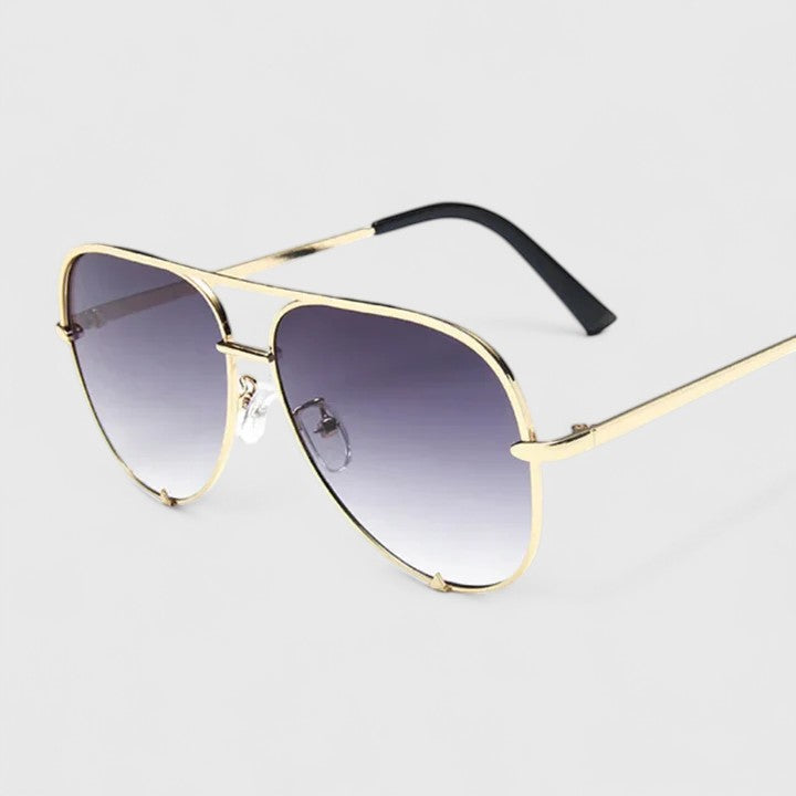 A woman by the sea wearing aviator sunglasses with gradient mirror lenses, relaxed in the sun.